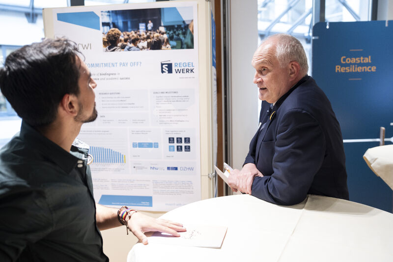 Zwei Personen im Gespräch vor einem RegelWerk-Poster bei der Jubiläumsveranstaltung des Leibniz-Europa-Büros.